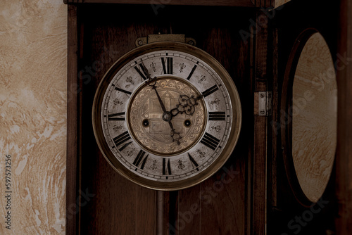 Old wooden clock with a pendulum hanging on the wall 