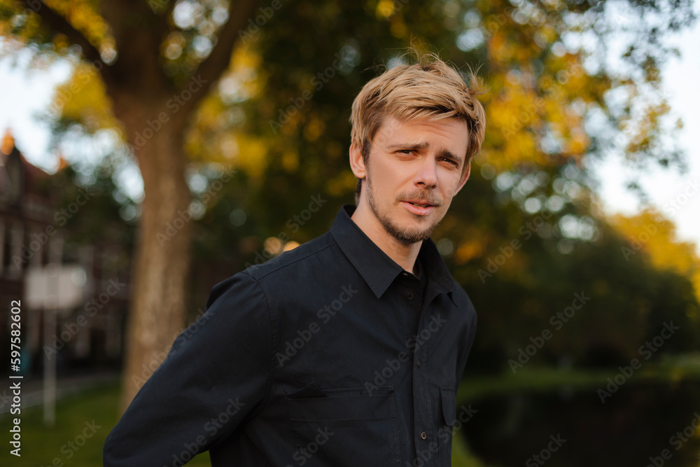 Young fun man wear black shirt and t-shirt walking rest relax in spring or summer green city park go down alley sunshine lawn outdoors on nature. Urban lifestyle leisure concept. Blonde man look calm. Young fun man wear black shirt and t-shirt walking rest relax in spring or summer green city park go down alley sunshine lawn outdoors on nature. Urban lifestyle leisure concept. Blonde man look calm.
