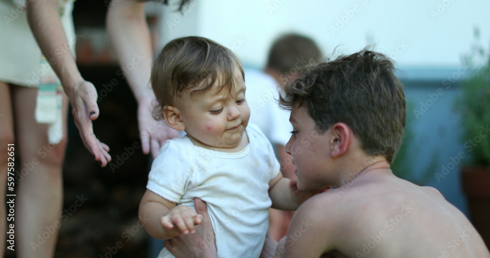 Candid older brother caring for baby sibling. Real life family moment between two brothers together Candid older brother caring for baby sibling. Real life family moment between two brothers together