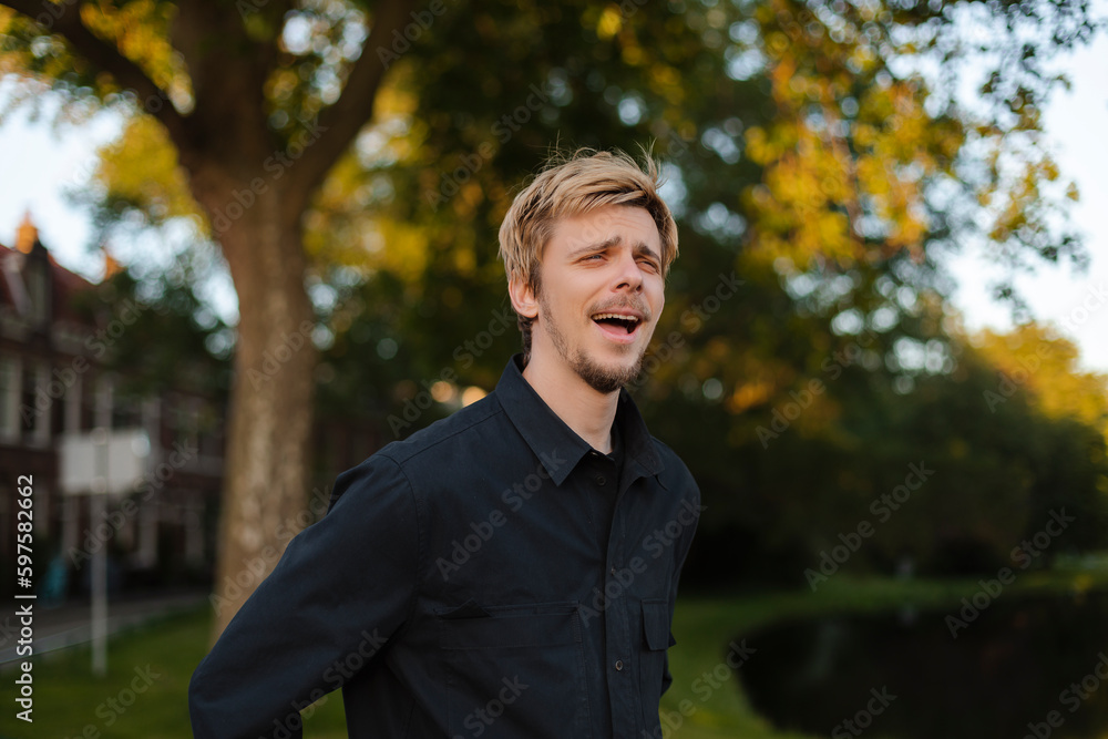 Young fun man wear black shirt and t-shirt walking rest relax in spring or summer green city park go down alley sunshine lawn outdoors on nature. Urban lifestyle leisure concept. Blonde man laughing Young fun man wear black shirt and t-shirt walking rest relax in spring or summer green city park go down alley sunshine lawn outdoors on nature. Urban lifestyle leisure concept. Blonde man laughing
