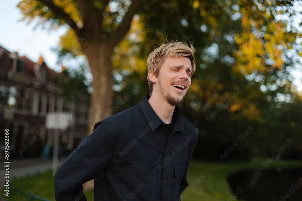 Young fun man wear black shirt and t-shirt walking rest relax in spring or summer green city park go down alley sunshine lawn outdoors on nature. Urban lifestyle leisure concept. Blonde man laughing Young fun man wear black shirt and t-shirt walking rest relax in spring or summer green city park go down alley sunshine lawn outdoors on nature. Urban lifestyle leisure concept. Blonde man laughing