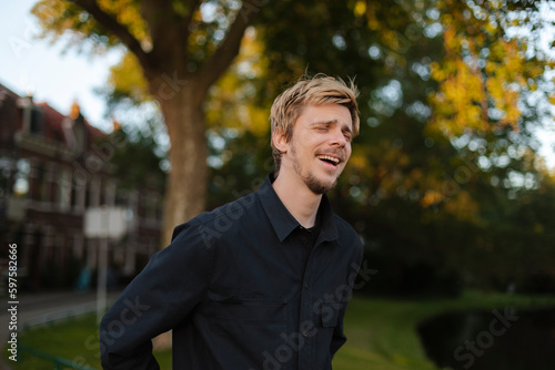 Young fun man wear black shirt and t-shirt walking rest relax in spring or summer green city park go down alley sunshine lawn outdoors on nature. Urban lifestyle leisure concept. Blonde man laughing