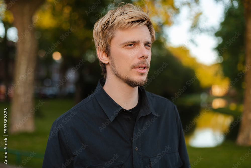 Young fun man wear black shirt and t-shirt walking rest relax in spring or summer green city park go down alley sunshine lawn outdoors on nature. Urban lifestyle leisure concept. Blonde man look calm. Young fun man wear black shirt and t-shirt walking rest relax in spring or summer green city park go down alley sunshine lawn outdoors on nature. Urban lifestyle leisure concept. Blonde man look calm.