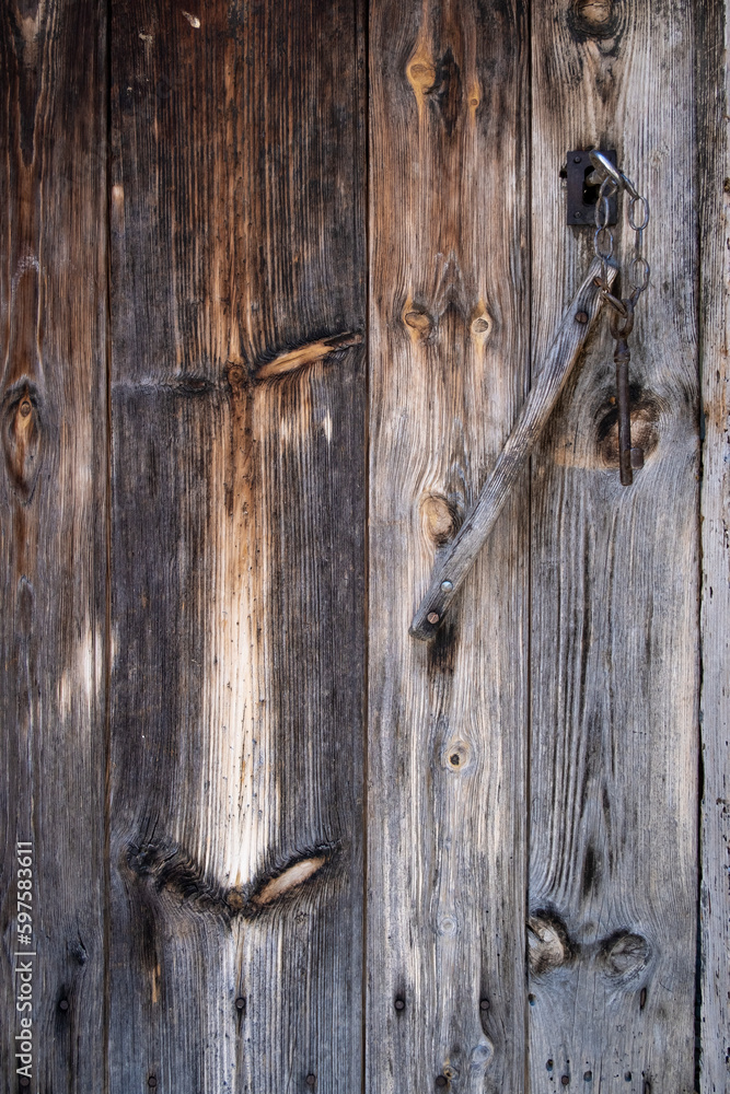 an old wooden door, weathered by the passage of time with an antique key inserted in the lock, worn wooden texture an old wooden door, weathered by the passage of time with an antique key inserted in the lock, worn wooden texture