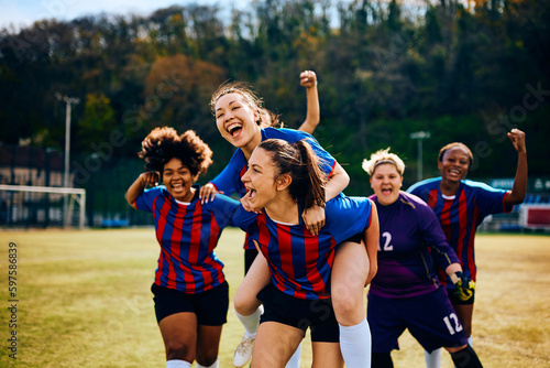 Excited teammates celebrate victory during women's soccer match on playing field. © Drazen