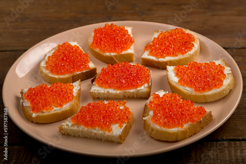 Canape with red caviar in butter on a beige plate.