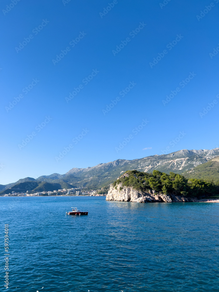 Small boat floats on the sea along the rocky shore