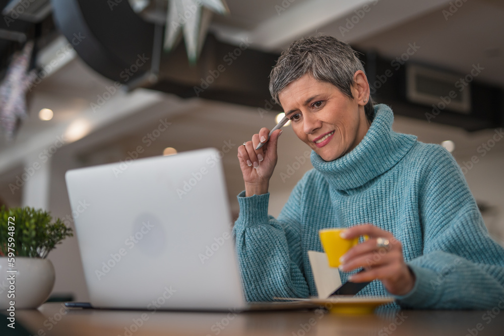 Fototapeta premium One senior woman sitting and drinking coffee while working on laptop casual clothing modern business woman concept 