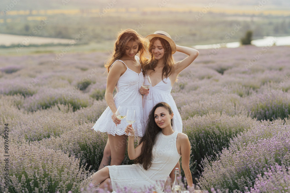Fototapeta premium Happy young friends having picnic on the lavender field. They are all happy, having fun, smiling, drinking wine and enjoying beautiful sunset and landscape. Friends enjoying picnic day.