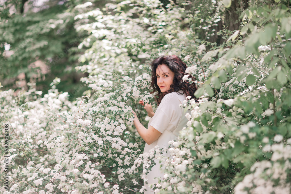 Woman spirea flowers. Portrait of a curly happy woman in a flowering bush with white spirea flowers.