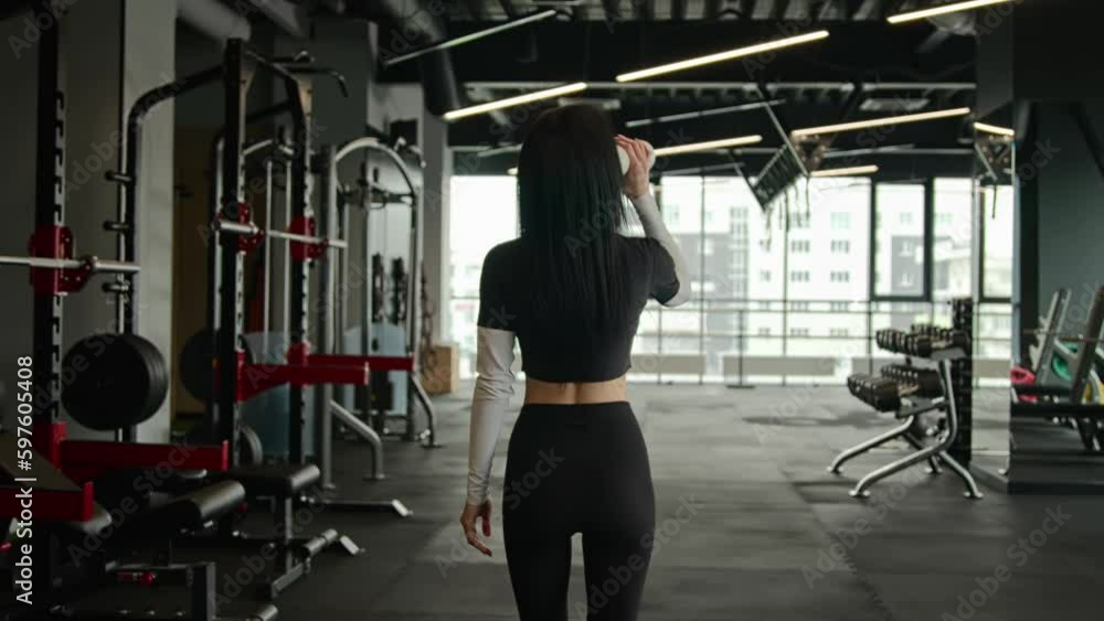 Back view unknown fit sportswoman girl athletic slim woman personal fitness trainer workout instructor walking in gym with sports equipment client of sport club going drink water drinking from bottle Back view unknown fit sportswoman girl athletic slim woman personal fitness trainer workout instructor walking in gym with sports equipment client of sport club going drink water drinking from bottle