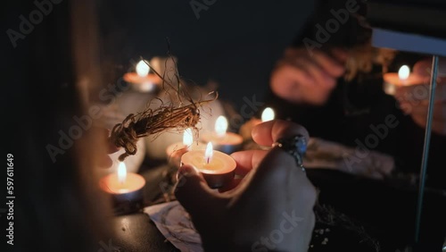 A sorceress or witch performs a rite or a love spell in a dark room with burning candles, close-up