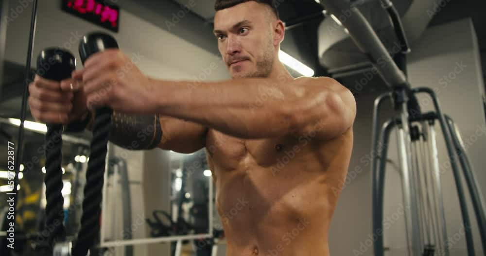 Young handsome man doing exercises on vertical row machine, hands, back workout. Sports facilities, man, woman exercising in gym in the background Young handsome man doing exercises on vertical row machine, hands, back workout. Sports facilities, man, woman exercising in gym in the background