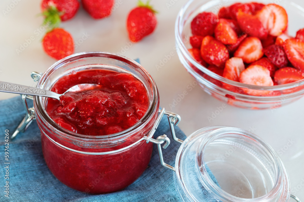 Glass jar with strawberry jam prepared for canning and fresh strawberries in a bowl on the table Glass jar with strawberry jam prepared for canning and fresh strawberries in a bowl on the table