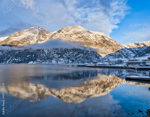 Waterfront buildings in Eidfjord village and mountains at sunset during winter on Hardangerfjord, Norway