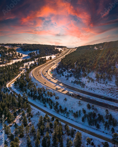 amazing sunrise shot in an alpine landscape with snow on hills and large highway bend passing through frame from a drone