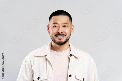 Smiling Korean male looking at camera isolated on gray background. Handsome young guy in studio