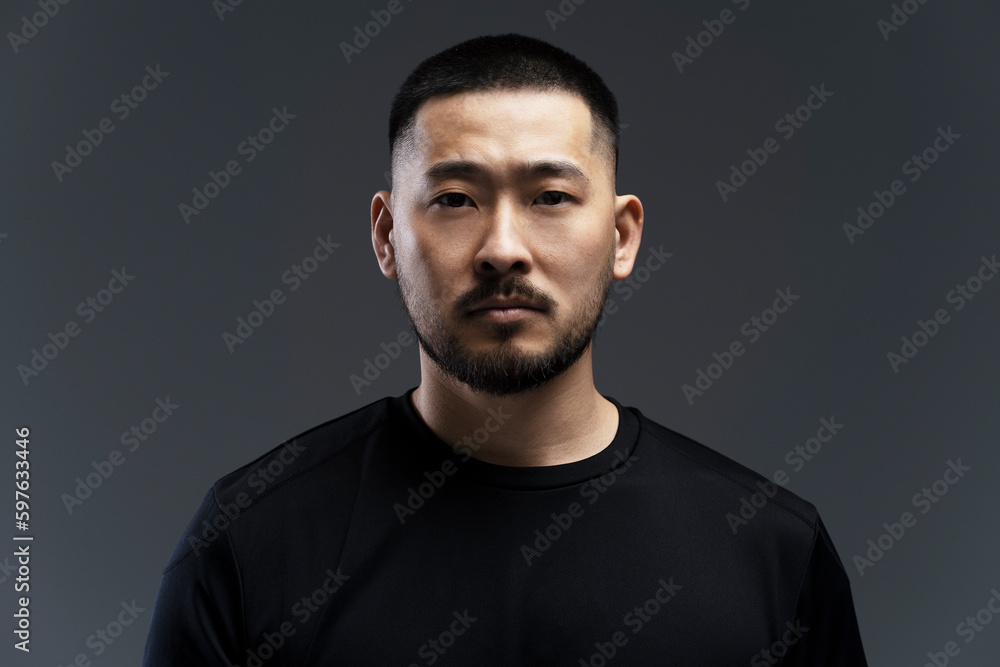 Serious, emotional young Asian man standing isolated on gray background, looking at camera