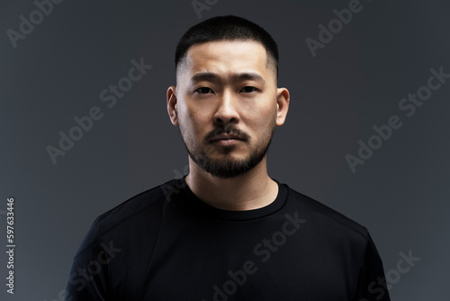 Serious, emotional young Asian man standing isolated on gray background, looking at camera © Maria Vitkovska