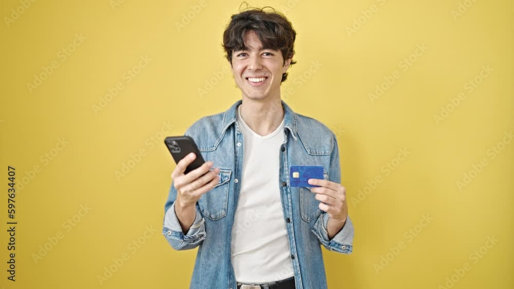 Young hispanic man shopping with smartphone and credit card over isolated yellow background Young hispanic man shopping with smartphone and credit card over isolated yellow background