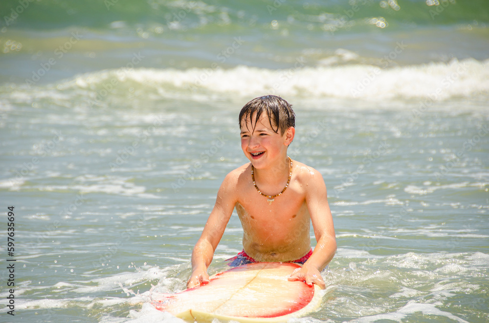 Happy young beach boy with his surfboard in the water Happy young beach boy with his surfboard in the water