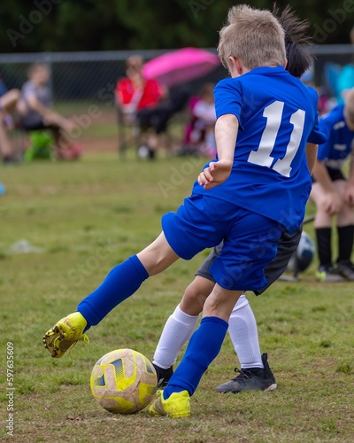 Young boy playing team soccer in blue uniform dribbling ball with feet