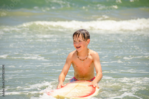 Photography Happy young beach boy with his surfboard in the water