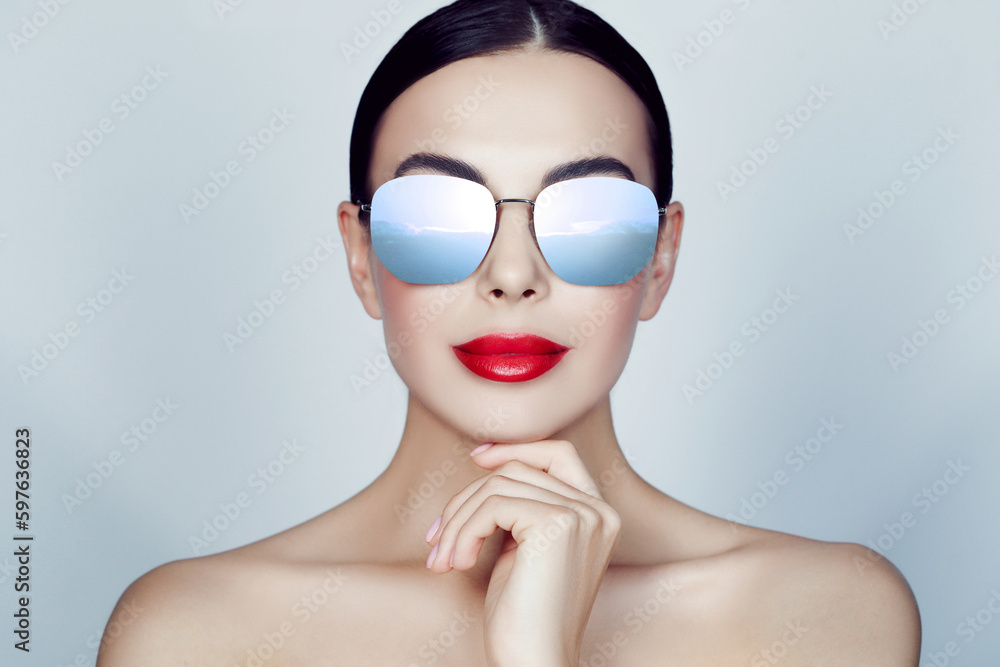 Attractive woman in stylish sunglasses on light grey background. Sky with clouds reflecting in lenses Attractive woman in stylish sunglasses on light grey background. Sky with clouds reflecting in lenses