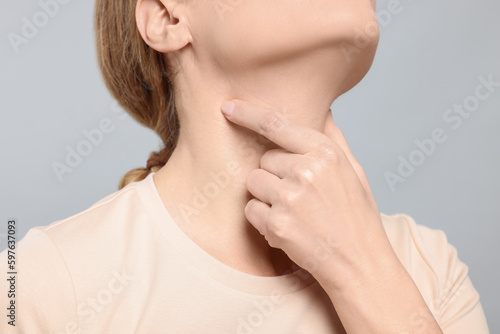Woman suffering from sore throat on light grey background, closeup