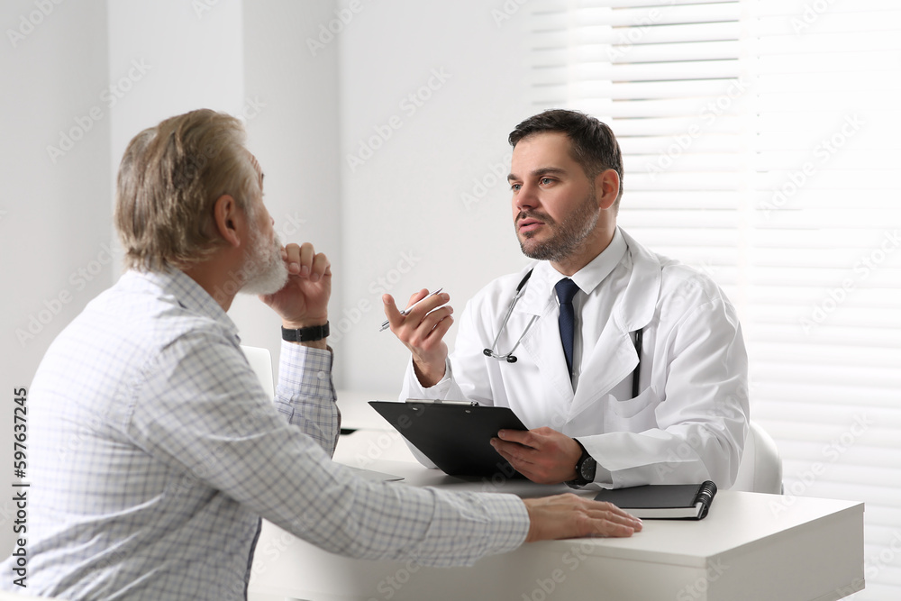Doctor consulting senior patient at white table in clinic Doctor consulting senior patient at white table in clinic
