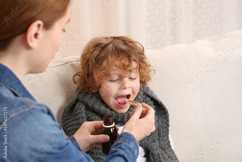 Photo Mother giving cough syrup to her son on sofa indoors