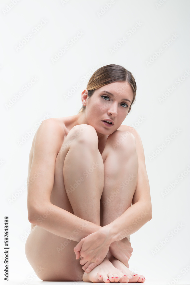 beauty concept - naked woman crouching hugs her own legs beauty concept - naked woman crouching hugs her own legs