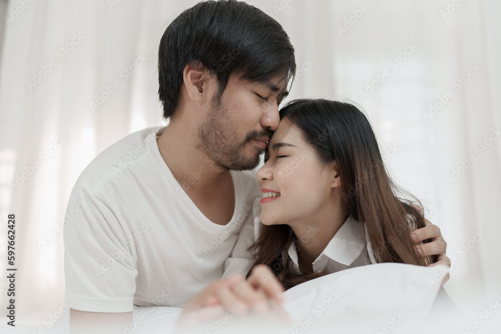 Asian Romantic couple in bed enjoying sensual foreplay Happy sensual young couple lying in bed together. Beautiful loving couple kissing in bed.