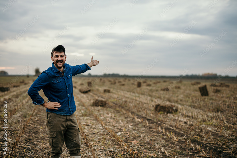 Portrait of a smiling male farmer in working outfit standing in his agricultural land and welcoming and showing his property, Copy space Portrait of a smiling male farmer in working outfit standing in his agricultural land and welcoming and showing his property, Copy space