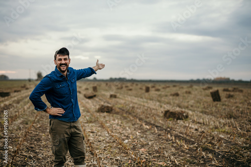 Portrait of a smiling male farmer in working outfit standing in his agricultural land and welcoming and showing his property, Copy space © La Famiglia