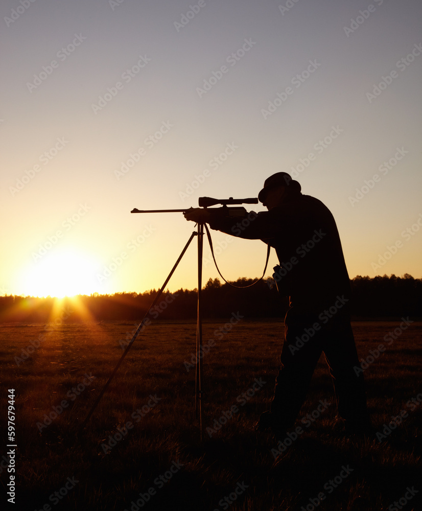 Hunting at sunset, man with rifle stand in nature to hunt game for sport on safari adventure. Sky, silhouette and hunter with gun, focus on target and evening setting sun for shooting hobby in bush.