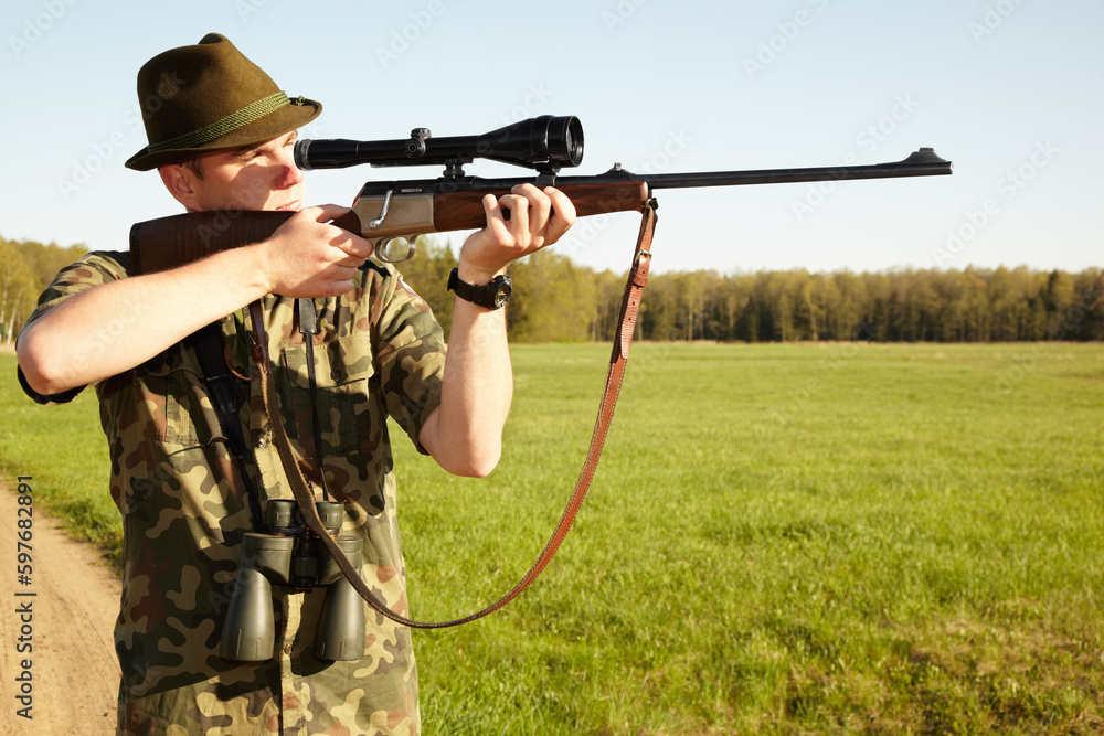 Fototapeta premium Hunter, gun and man in nature on a Africa safari for animal shooting with a weapon on vacation. Hunting sport, male person and target hunt practise of a traveler in camouflage looking at a scope