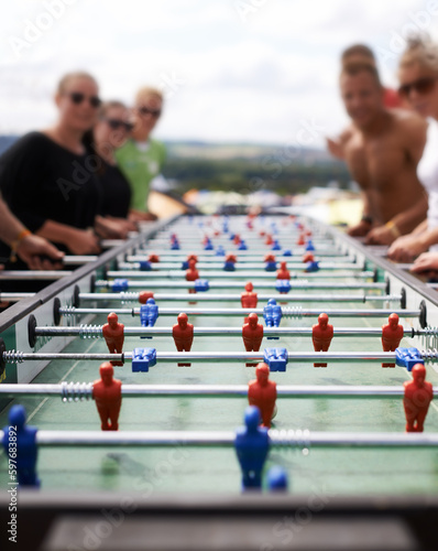 Friends playing with a foosball at a party for competition, fun skill or sports event. Celebration, activity and group of people enjoying a football table game or match for a friendly championship.