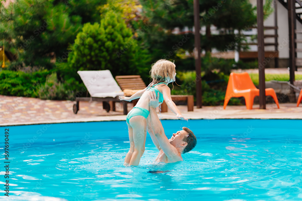 Dad and daughter play in the pool. dad throws daughter in the air.