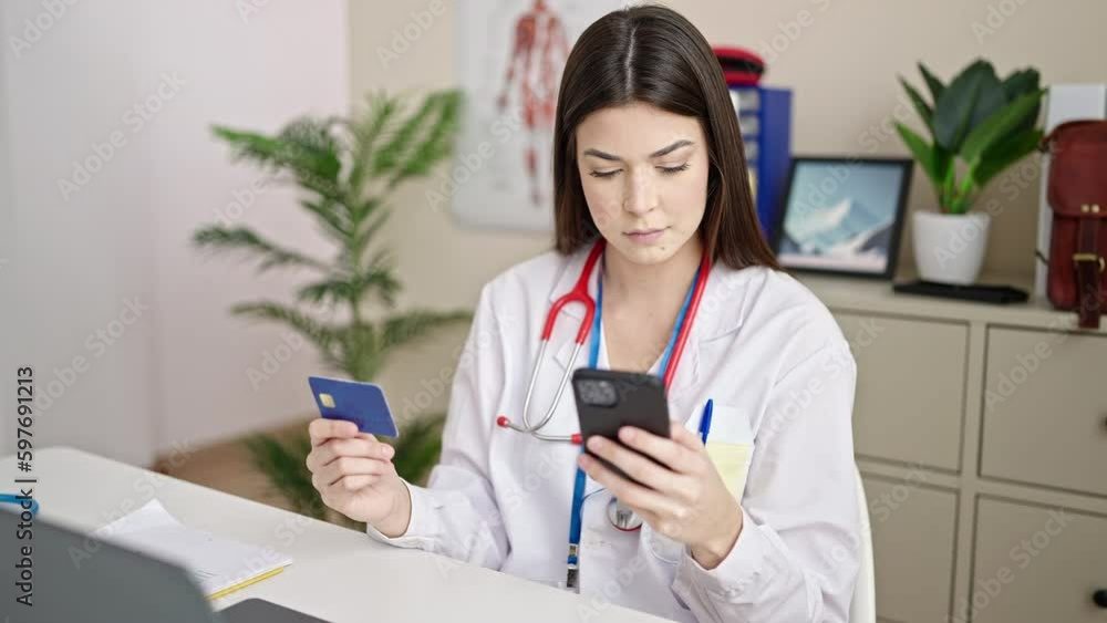 Young beautiful hispanic woman doctor shopping with credit card and smartphone at clinic Young beautiful hispanic woman doctor shopping with credit card and smartphone at clinic