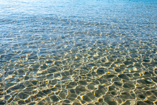 Transparent calm blue sea water background, texture. Sunlight reflects on ocean, sandy seabed. Space