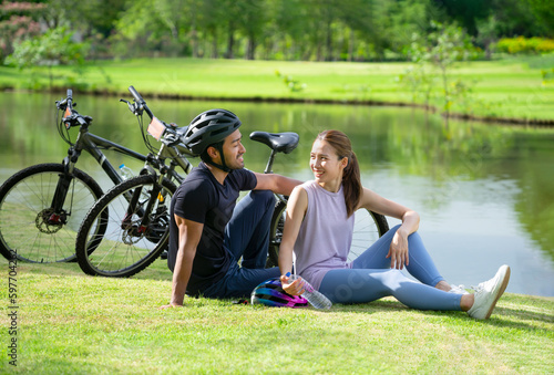 Asian couple talking and laughing happily,young romantic couple relaxing on the lawn by the park pond after cycling,concept for family lifestyle,activity,relationship,the love of family