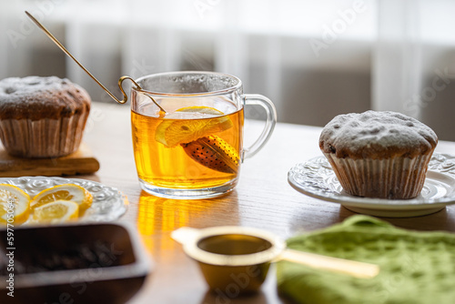 A cup of tea with lemon and cupcakes on a table near the window, backlight.