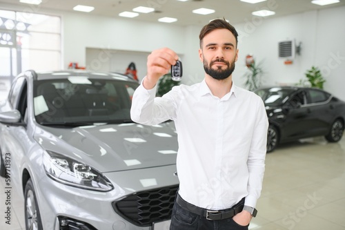 Happy young guy checking new luxury car, buying automobile at dealership centre. Portrait of cheerful millennial Caucasian man examining auto at showroom store