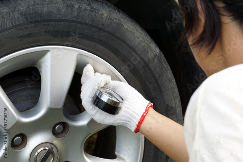 Woman checking the pressure of an old car tire with a tire pressure gauge for safety and assurance before use.