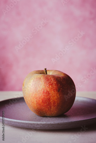 Apfel au Teller vor rosa Hintergrund