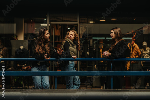 Three girls discussing fashion while leaning on a blue fence at the shopping mall. Front view shot