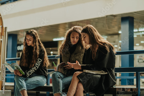 Wallpaper Mural Beautiful curly haired girl looking at her friend phone and writing some notes down in the notebook. Their long haired brunette friend is reading a book Torontodigital.ca