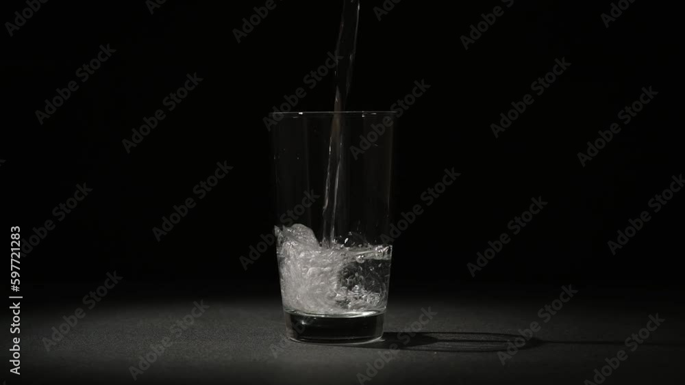 Clean drinking water is poured into a glass glass on a black background. Clean drinking water is poured into a glass glass on a black background.