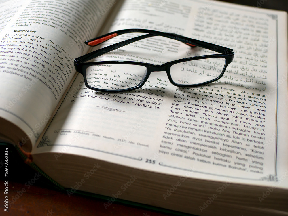 Black reading glasses on the islamic book with bokeh background, shallow focus Black reading glasses on the islamic book with bokeh background, shallow focus